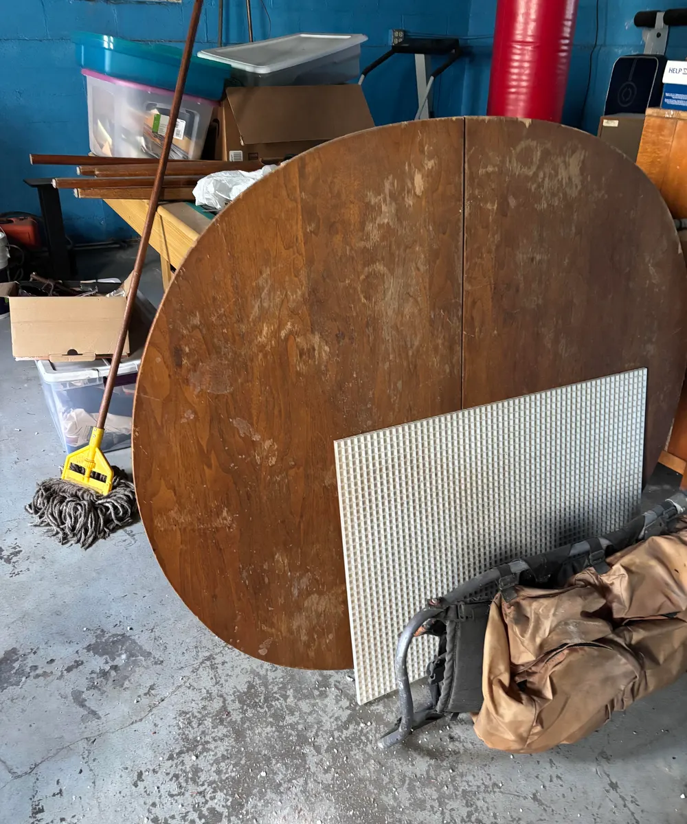Round wooden dining table, egg-crate ceiling panel, storage bins and an old pack frame in a blue-painted Chicago basement