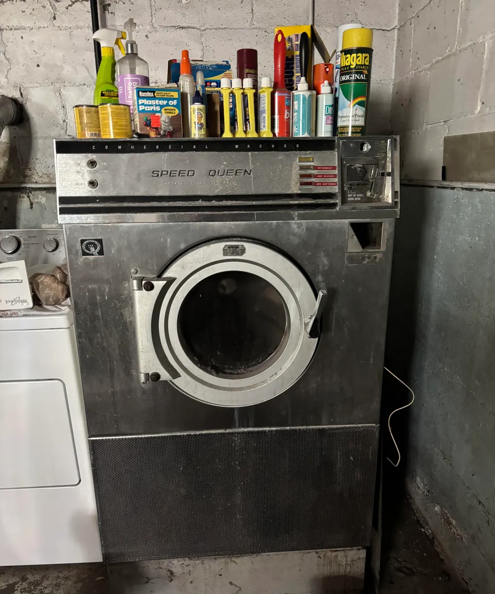 Stainless-steel coin-op Speed Queen commercial washer with cleaning supplies on top in a Chicago basement