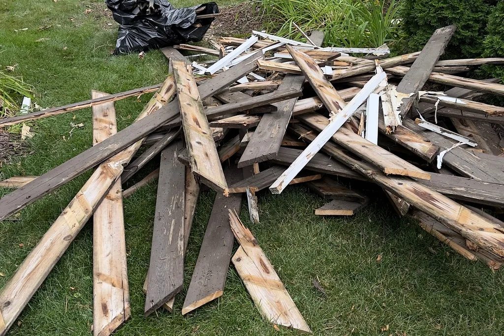 Pile of weathered wood boards and white trim on a backyard lawn in Wheaton, IL, staged for construction debris removal